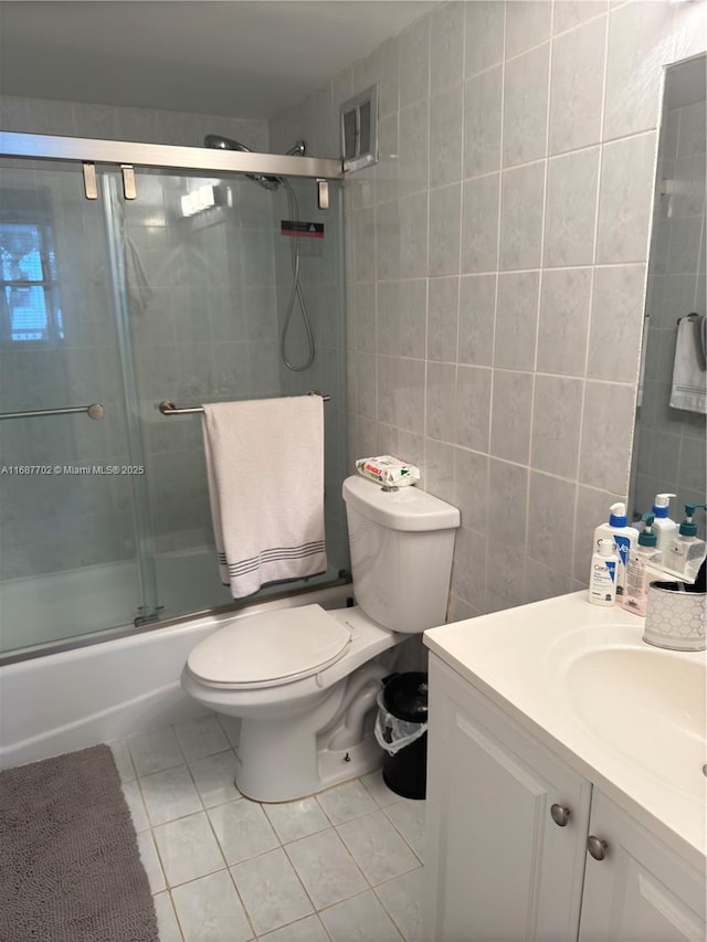 full bathroom featuring shower / bath combination with glass door, tile walls, tile patterned flooring, vanity, and toilet