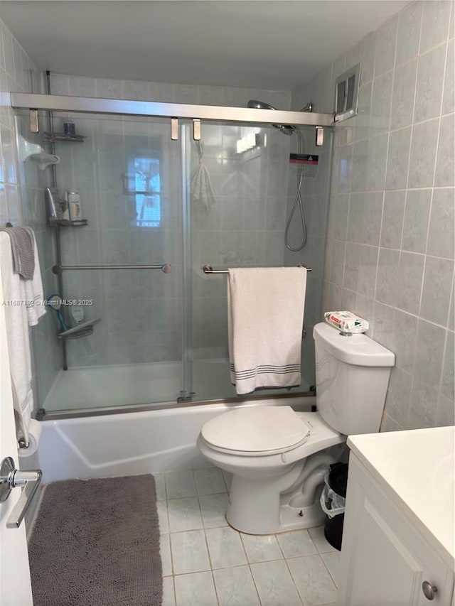 full bathroom featuring shower / bath combination with glass door, tile walls, vanity, tile patterned floors, and toilet