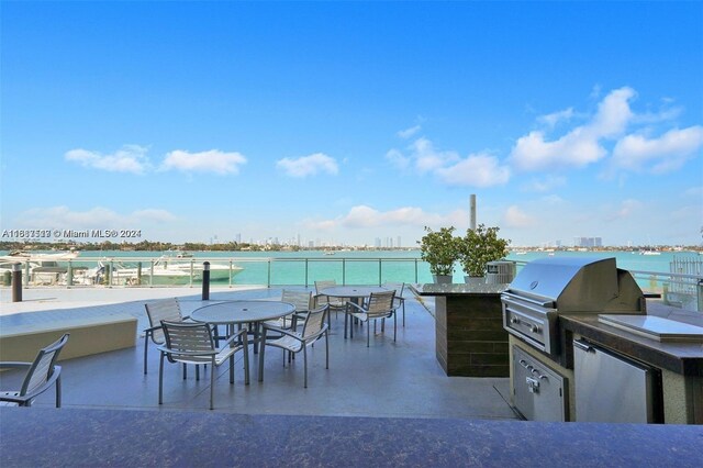 view of patio with area for grilling, a water view, and an outdoor kitchen