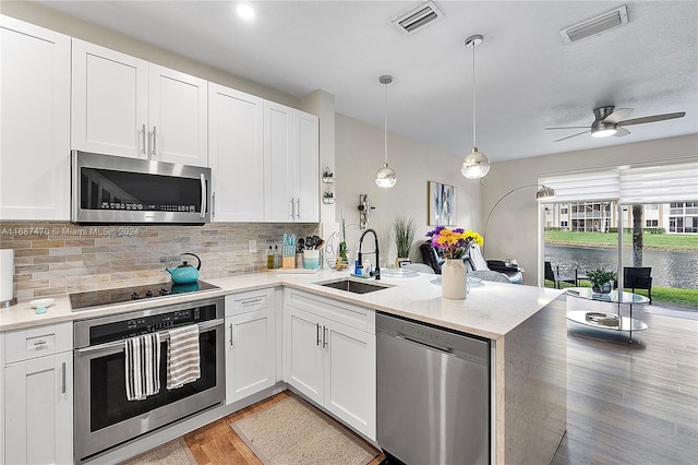 kitchen featuring appliances with stainless steel finishes, white cabinetry, light stone countertops, pendant lighting, and sink