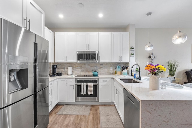 kitchen with white cabinets, hanging light fixtures, stainless steel appliances, and light wood-type flooring