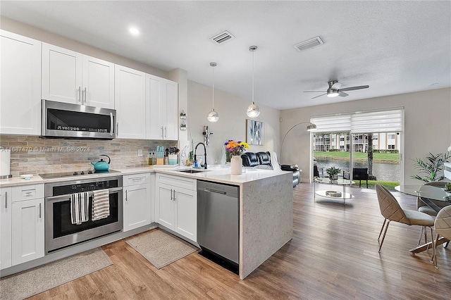 kitchen featuring kitchen peninsula, white cabinets, light hardwood / wood-style flooring, pendant lighting, and stainless steel appliances