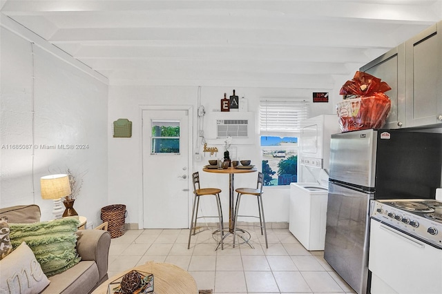 kitchen with white gas stove, beamed ceiling, stacked washer / drying machine, light tile patterned floors, and stainless steel fridge