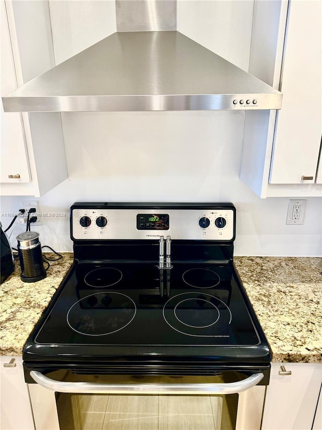 kitchen with electric range, white cabinets, light stone counters, and wall chimney range hood