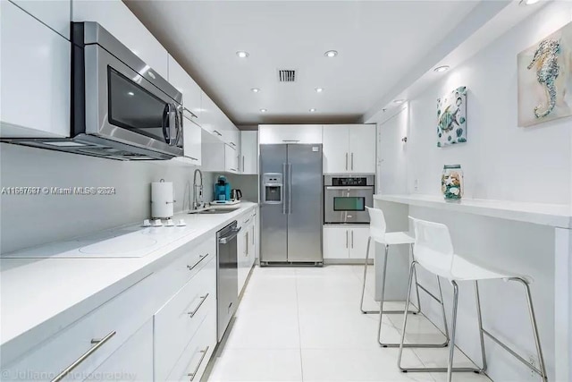 kitchen with sink, a breakfast bar, white cabinets, light tile patterned floors, and appliances with stainless steel finishes