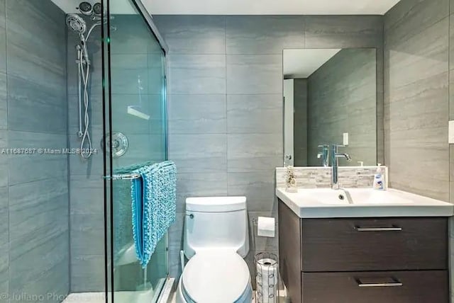 bathroom featuring vanity, toilet, tile walls, and a shower with shower door