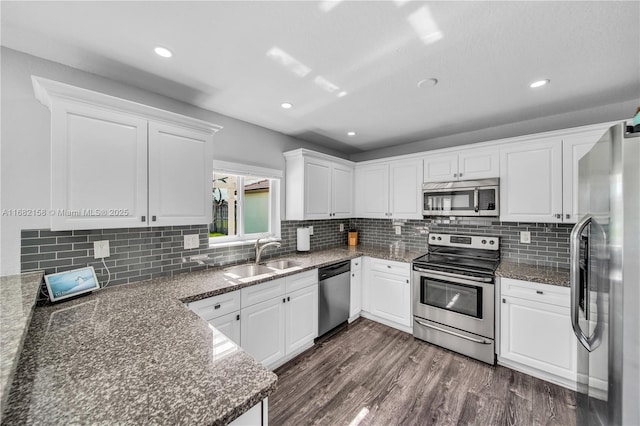 kitchen featuring sink, appliances with stainless steel finishes, dark stone countertops, dark hardwood / wood-style floors, and white cabinets