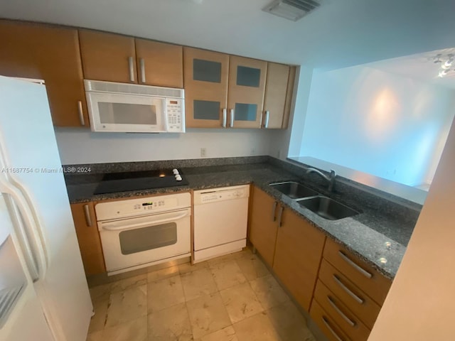 kitchen with sink, white appliances, and dark stone countertops