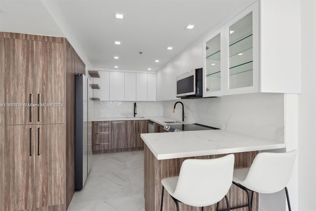 kitchen with decorative backsplash, a breakfast bar area, kitchen peninsula, white cabinets, and appliances with stainless steel finishes