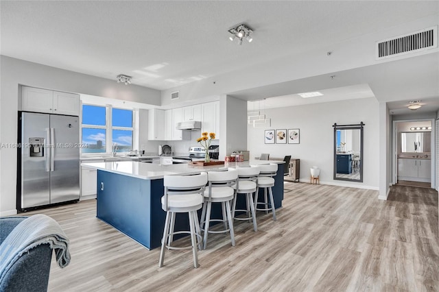 kitchen featuring white cabinets, a kitchen island, a kitchen bar, light wood-type flooring, and stainless steel appliances