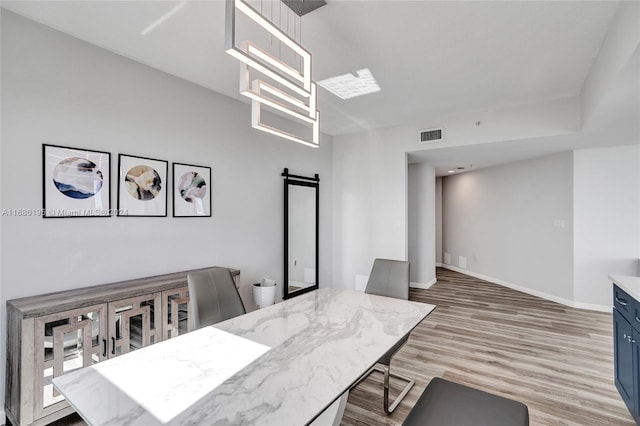 dining area featuring a barn door, a notable chandelier, and light wood-type flooring