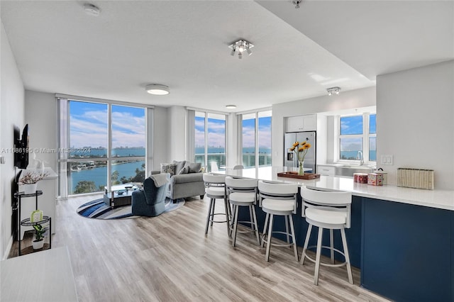 kitchen with a kitchen breakfast bar, light hardwood / wood-style flooring, stainless steel refrigerator with ice dispenser, a wall of windows, and a water view