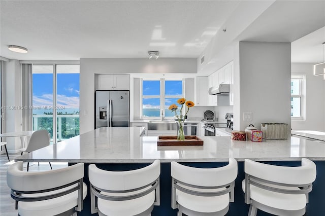 kitchen with light stone counters, appliances with stainless steel finishes, a kitchen bar, and white cabinets