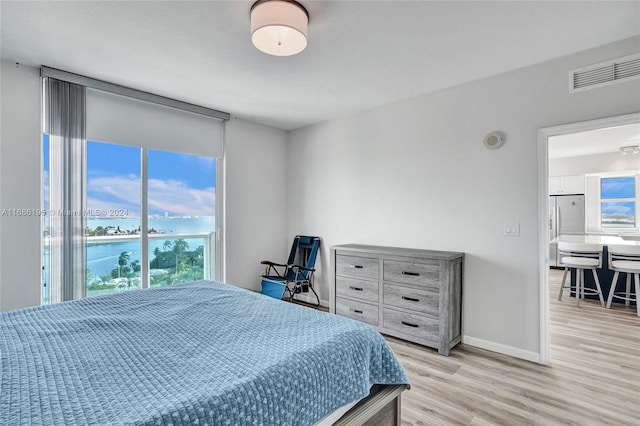 bedroom with a water view, light wood-type flooring, and fridge