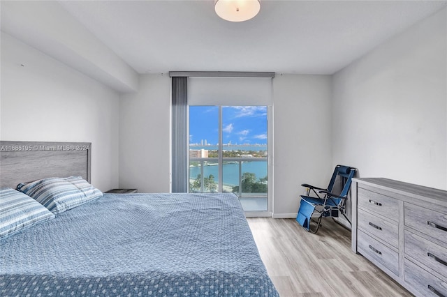 bedroom featuring light hardwood / wood-style floors, access to exterior, and a water view