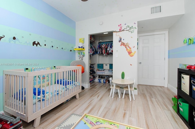 bedroom with a closet, a nursery area, and wood-type flooring