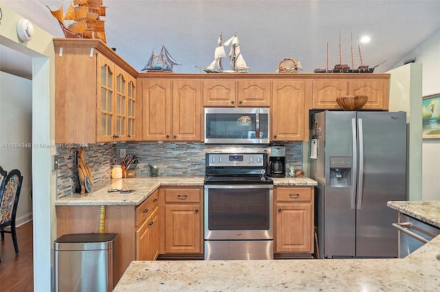 kitchen featuring light stone countertops, hardwood / wood-style flooring, appliances with stainless steel finishes, and decorative backsplash