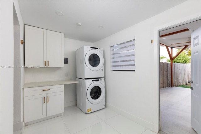 clothes washing area with stacked washer and clothes dryer, cabinets, light tile patterned floors, and ceiling fan