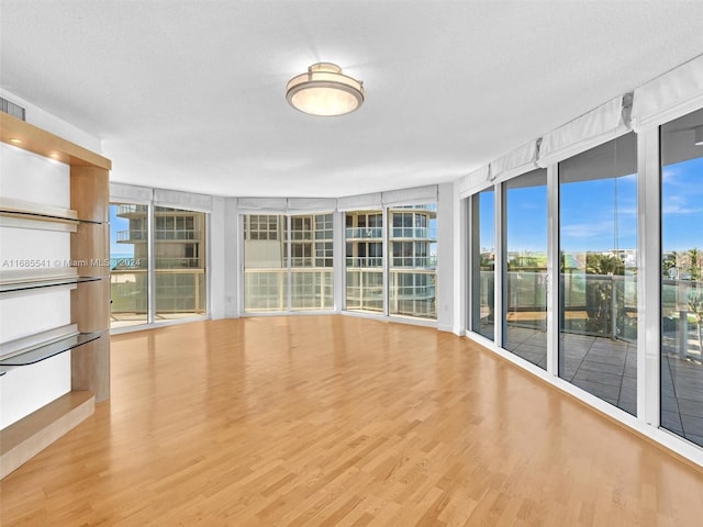 unfurnished living room with a wall of windows, a textured ceiling, and light wood-type flooring