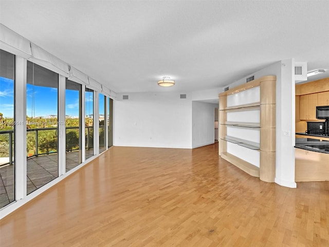 unfurnished living room featuring light hardwood / wood-style floors, a textured ceiling, and a wall of windows