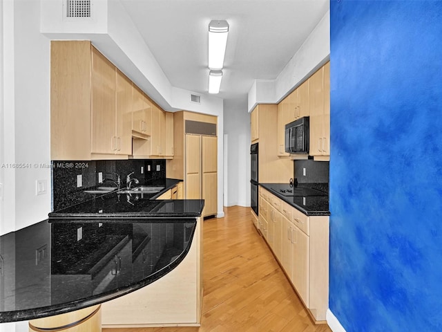 kitchen with kitchen peninsula, backsplash, dark stone counters, black appliances, and light wood-type flooring