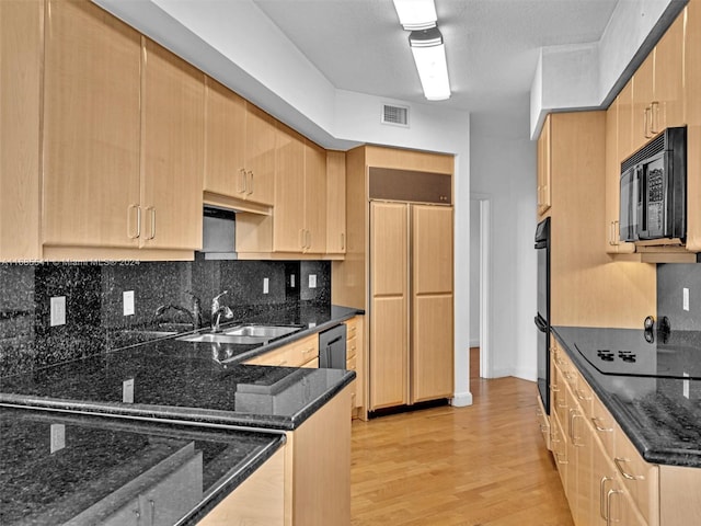 kitchen with decorative backsplash, dark stone countertops, sink, black appliances, and light hardwood / wood-style floors