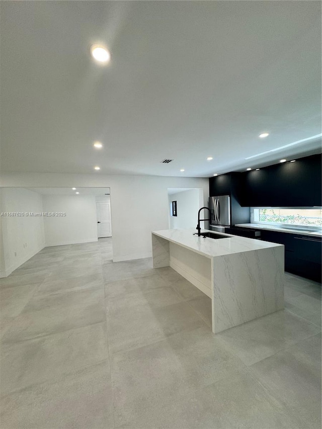 kitchen with a large island, sink, light stone counters, and stainless steel refrigerator