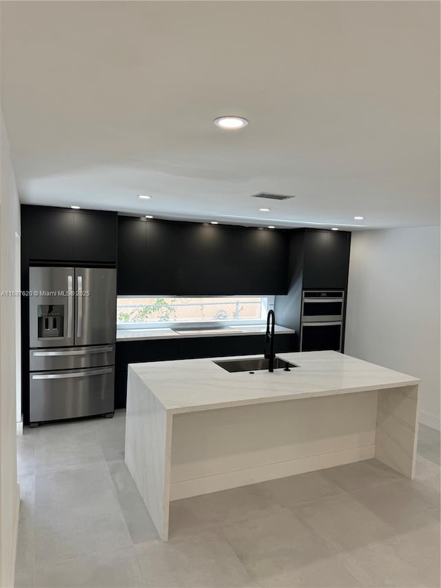 kitchen featuring sink, a breakfast bar area, a kitchen island with sink, stainless steel appliances, and light stone countertops