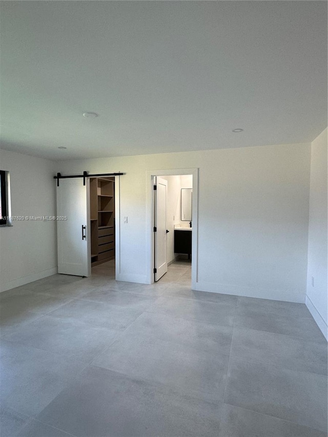 unfurnished bedroom featuring ensuite bathroom and a barn door