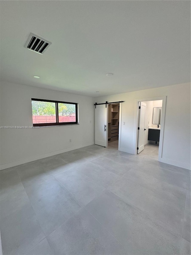 unfurnished bedroom featuring ensuite bathroom, a barn door, and a spacious closet