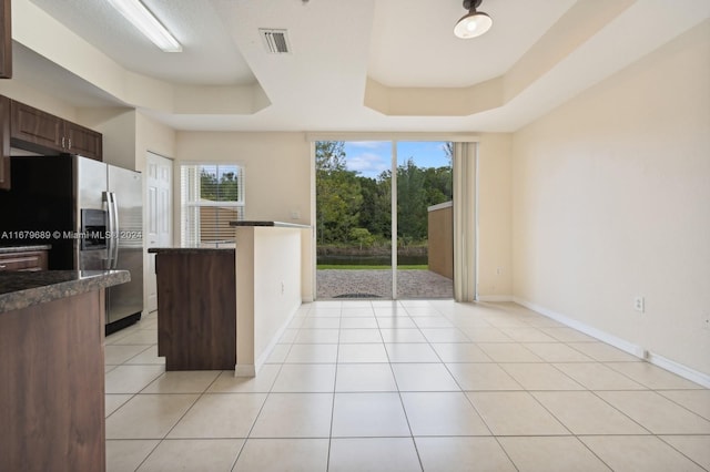 kitchen featuring dark brown cabinets, stainless steel refrigerator with ice dispenser, a tray ceiling, and light tile patterned floors