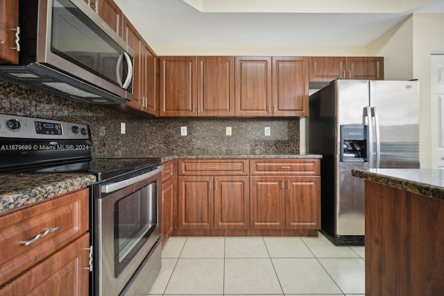 kitchen with dark stone countertops, backsplash, stainless steel appliances, and light tile patterned floors