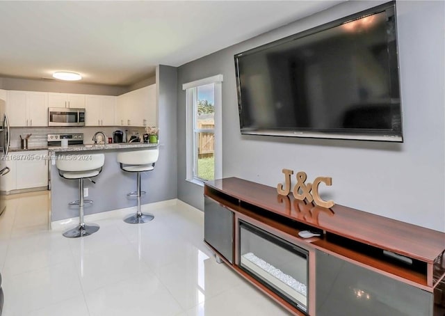 kitchen featuring a breakfast bar area, stainless steel appliances, sink, light tile patterned flooring, and white cabinets