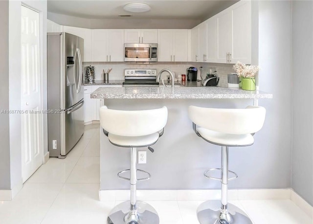 kitchen with light tile patterned flooring, backsplash, a kitchen breakfast bar, stainless steel appliances, and white cabinets