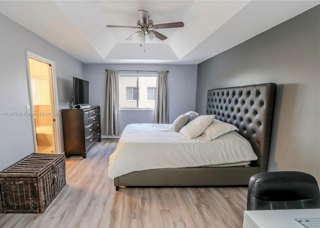 bedroom featuring ceiling fan, a raised ceiling, light hardwood / wood-style flooring, and ensuite bathroom