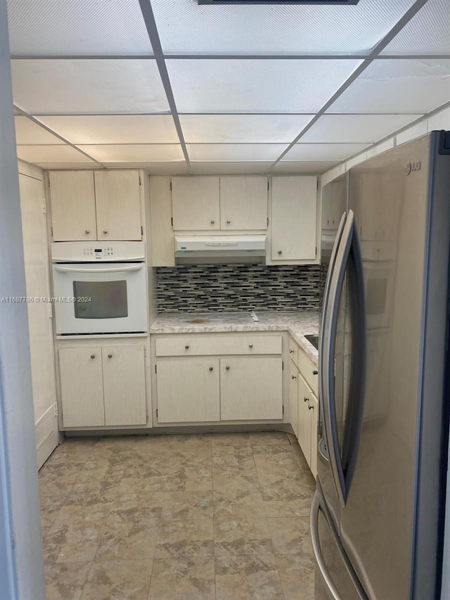 kitchen featuring oven, decorative backsplash, stainless steel refrigerator, and cream cabinetry