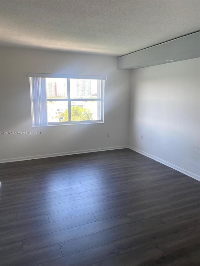 spare room featuring dark wood-type flooring and a textured ceiling