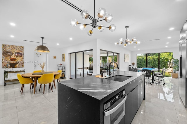 kitchen featuring pool table, a center island with sink, sink, oven, and decorative light fixtures