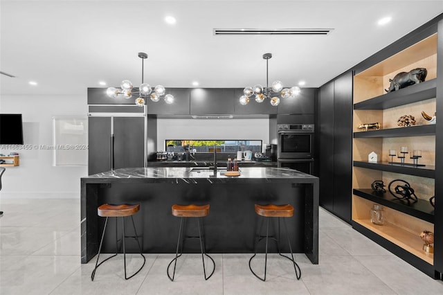 kitchen featuring dark stone countertops, stainless steel double oven, decorative light fixtures, and a breakfast bar