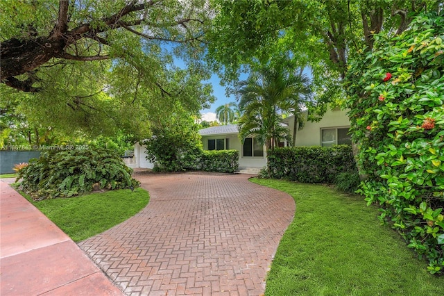 view of front of home with decorative driveway, a front lawn, and stucco siding