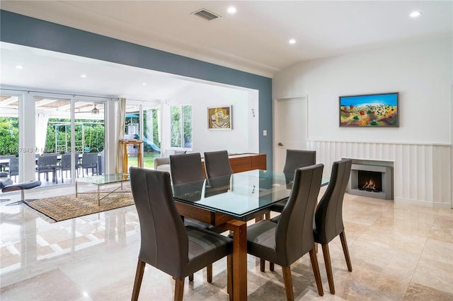 dining space with lofted ceiling, a warm lit fireplace, visible vents, and recessed lighting