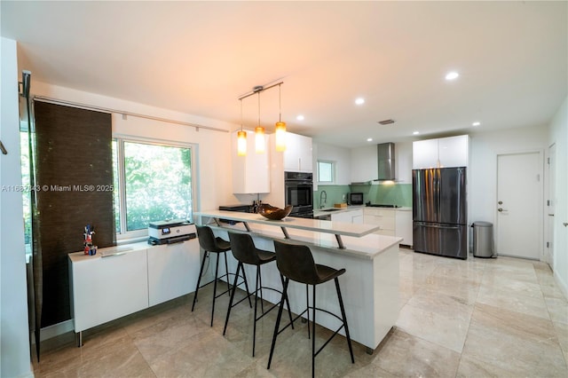 kitchen with wall chimney exhaust hood, a peninsula, light countertops, black appliances, and white cabinetry