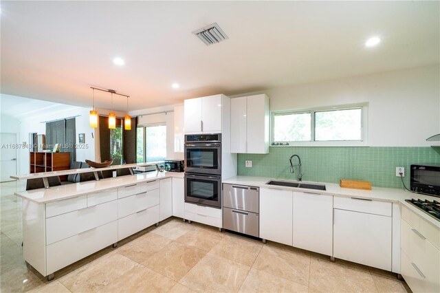 kitchen featuring visible vents, appliances with stainless steel finishes, white cabinetry, a sink, and a peninsula