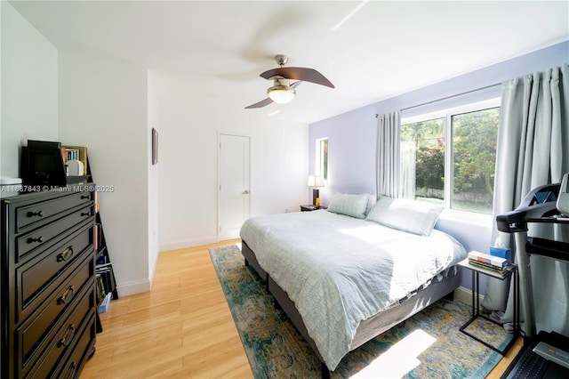 bedroom with light wood finished floors, a ceiling fan, and baseboards