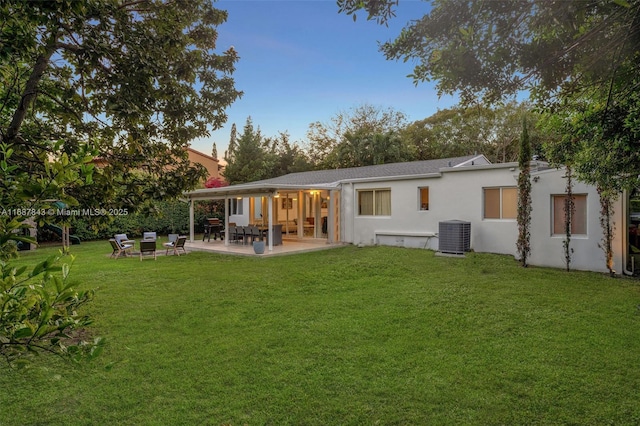 rear view of property featuring stucco siding, central AC, a lawn, and a patio