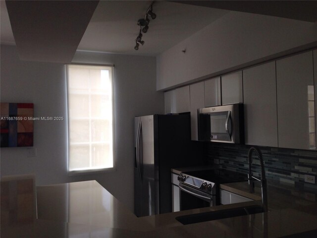 kitchen with appliances with stainless steel finishes, sink, kitchen peninsula, white cabinets, and decorative backsplash