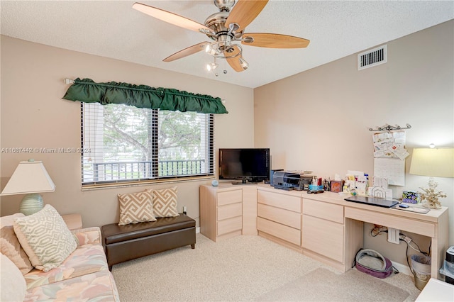 carpeted office with a textured ceiling, built in desk, and ceiling fan