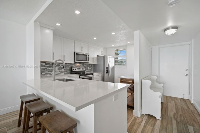 kitchen with kitchen peninsula, light hardwood / wood-style flooring, a kitchen breakfast bar, white cabinetry, and appliances with stainless steel finishes