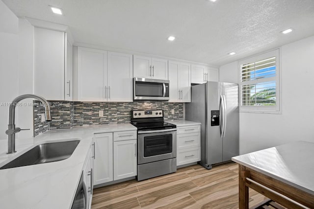 kitchen with light hardwood / wood-style floors, white cabinetry, sink, appliances with stainless steel finishes, and tasteful backsplash