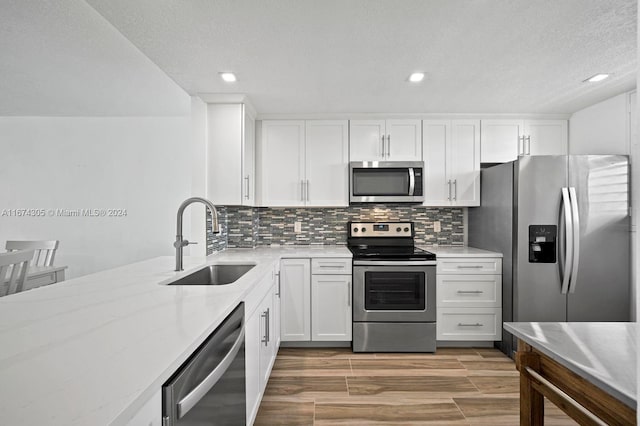 kitchen with stainless steel appliances, hardwood / wood-style floors, sink, backsplash, and white cabinetry